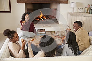 Family Sitting On Sofa In Lounge Next To Open Fire Eating Pizza