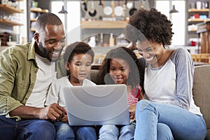 Family Sitting On Sofa In Open Plan Lounge Using Laptop