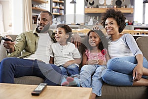 Family Sitting On Sofa In Open Plan Lounge Watching Television