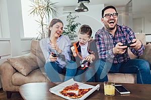 Family sitting on a sofa and playing video games and eating pizza