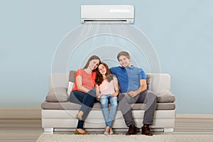 Family Sitting On Sofa Under Air Conditioning