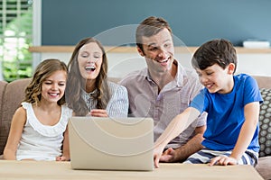 Family sitting on sofa using laptop in living room at home