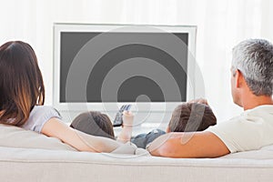 Family sitting on sofa watching television together