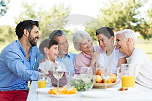 Family sitting at table outdoors, smiling