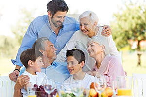 Family sitting at table outdoors, smiling