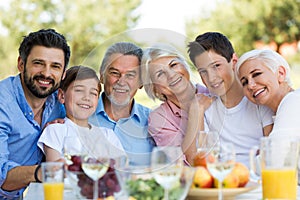 Family sitting at table outdoors, smiling