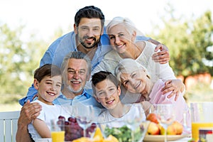 Family sitting at table outdoors, smiling