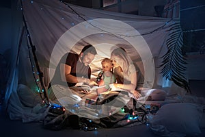 Family sitting in a teepee, reading stories with the flashlight