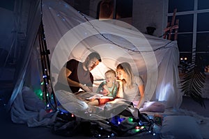 Family sitting in a teepee, reading stories with the flashlight