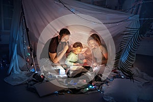 Family sitting in a teepee, reading stories with the flashlight