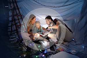 Family sitting in a teepee, reading stories with the flashlight