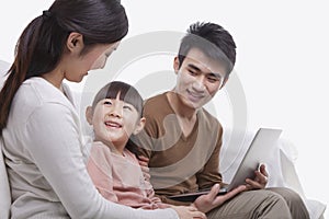 Family sitting together on the sofa using laptop, mother is looking at her smiling daughter, studio shot