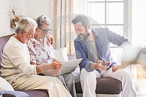 Family sitting together on the sofa using modern device laptop and phone and enjoying connection to web internet. Father mother