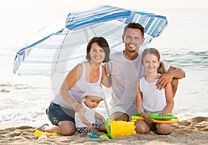 Family sitting under umbrella on the beach