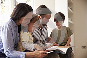 Family Sitting On Window Seat Reading Story At Home Together