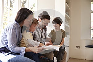 Family Sitting On Window Seat Reading Story At Home Together