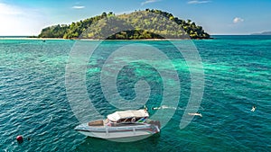 Family snorkeling near boat in clear tropical sea, aerial drone view from above, mother and kids snorkelers swimming in water