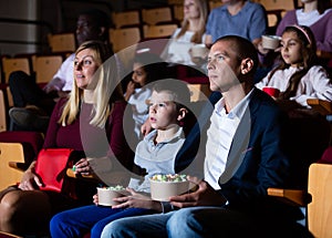 Family with son watching movie and eating popcorn in cinema