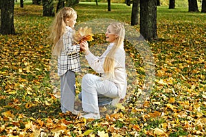 Family spend time together in autumn park. Mother and daughter picking a bouquet of yellow leaves