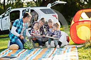 Family spending time together. Father reading book outdoor with kids against their suv car