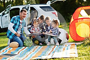 Family spending time together. Father reading book outdoor with kids against their suv car