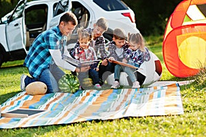 Family spending time together. Father reading book outdoor with kids against their suv car