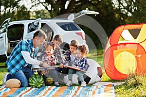 Family spending time together. Father reading book outdoor with kids against their suv car