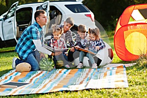 Family spending time together. Father reading book outdoor with kids against their suv car