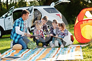 Family spending time together. Father reading book outdoor with kids against their suv car