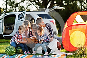 Family spending time together. Mother reading book outdoor with kids against their suv car