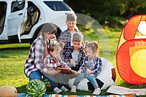 Family spending time together. Mother reading book outdoor with kids against their suv car