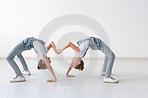 Family and sport concept - Two acrobat twin girls are standing on the hands over white background