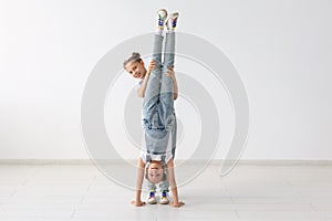 Family and sport concept - Two acrobat twin girls are standing on the hands over white background