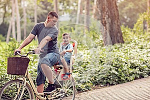 Family sport and healthy lifestyle- father and son riding a bicycle together outdoors in a city park.