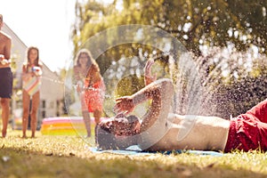 Family Squirting Father With Water Pistols In Summer Garden As He Sunbathes photo
