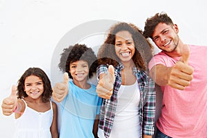 Family Standing Outdoors Against White Wall Giving Thumbs Up