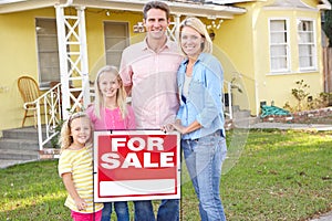 Family Standing By For Sale Sign Outside Home