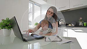 Family stress, multitasking mum with crying infant boy while working on laptop computer and talking on cell phone