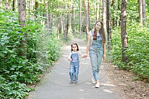 Family, summer and nature concept - Attractive young woman and beautiful little daughter girl walking in green park