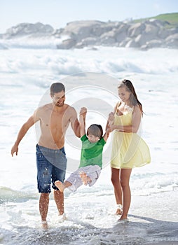 Family, summer and swinging child at beach for fun, travel or holiday with a smile in water. A man, woman and kid or son