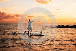 Family summer vacations. Silhouette of father and daughter surfing on a sup board. Sunset sky and sea of peach color at