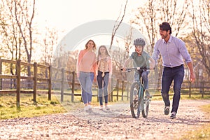 Family On Summer Walk In Countryside Teaching Son To Ride Bike