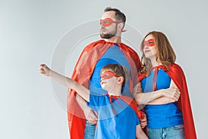 family of superheroes in masks and cloaks standing together and looking away