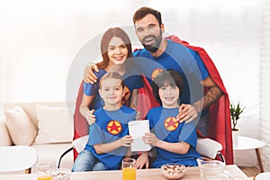 A family of superheroes sit at a table. The incredibles are posing in a bright room