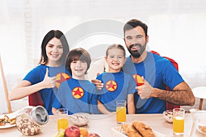 A family of superheroes sit at a table. The incredibles are posing in a bright room