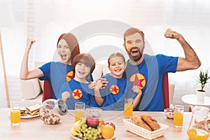 A family of superheroes sit at a table. The incredibles are posing in a bright room