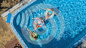 Family in swimming pool aerial drone view from above, happy mother and kids swim on inflatable ring donuts and have fun in water