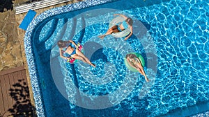 Family in swimming pool aerial drone view from above, happy mother and kids swim on inflatable ring donuts and have fun in water