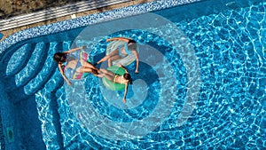 Family in swimming pool aerial drone view from above, happy mother and kids swim on inflatable ring donuts and have fun in water