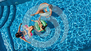 Family in swimming pool aerial drone view from above, happy mother and kids swim on inflatable ring donuts and have fun in water